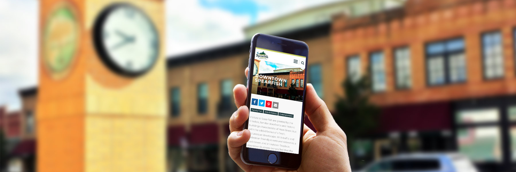 Visit Spearfish website on phone with a town background